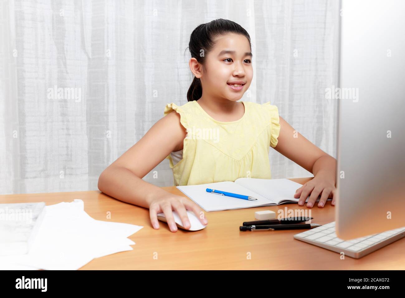 Ragazza giovane asiatica che usa la matita per fare i compiti da sola. Libro di scrittura del capretto dello studente. La ragazza usa il computer per studiare a casa. Istruzione a casa Foto Stock