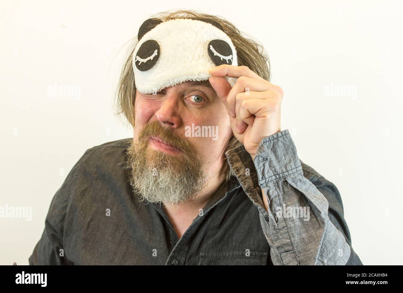 L'uomo con la barba toglie la maschera di sonno. L'uomo stanco sconvolto non ha abbastanza sonno, tocca faccia con mano, indossa la vista e, dormiva male di notte. Foto Stock