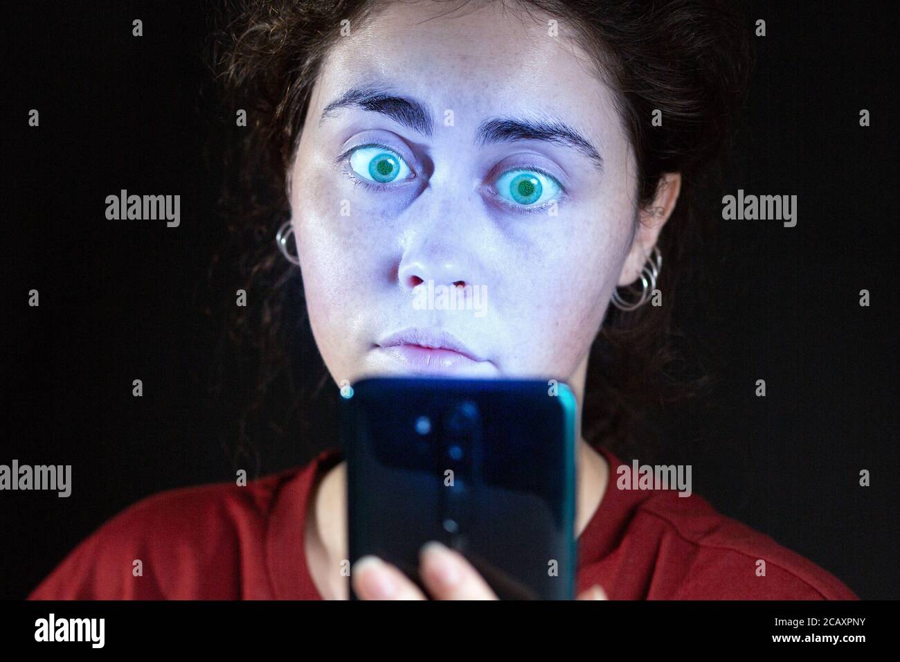 Primo piano ritratto di una donna che guarda il suo cellulare come una zombie. Sfondo nero. Il concetto di dipendenza online. Foto Stock