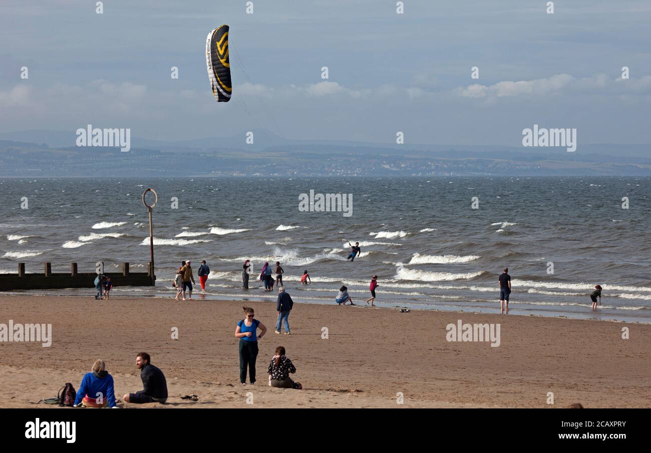 Portobello, Edimburgo, Scozia, Regno Unito. 9 agosto 2020. Kite Surfer in background con la spiaggia groyes.More persone sulla spiaggia nel tardo pomeriggio, il vento fresco che dà la rara opportunità di Kite Surf sul Firth of Forth a Porty. Foto Stock