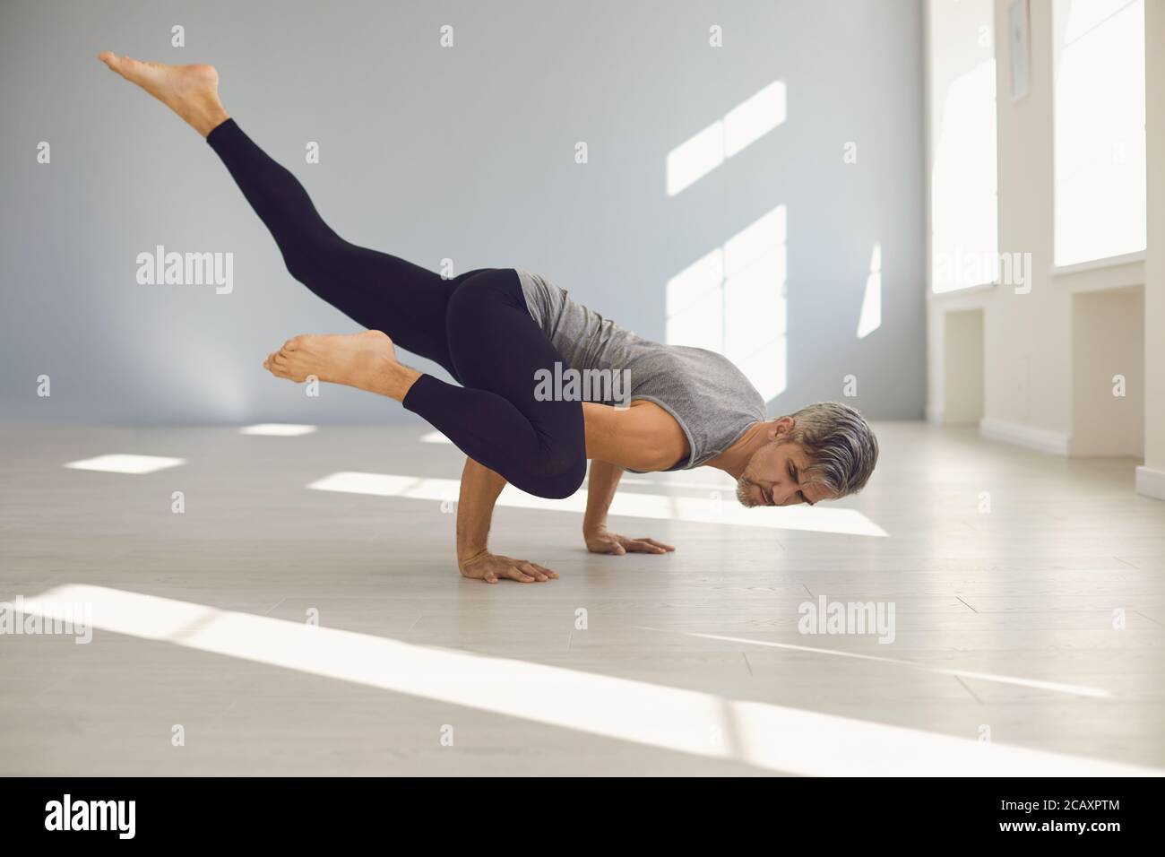 Uomo yoga. Un uomo sta praticando l'equilibrio dello yoga in una stanza grigia. Foto Stock