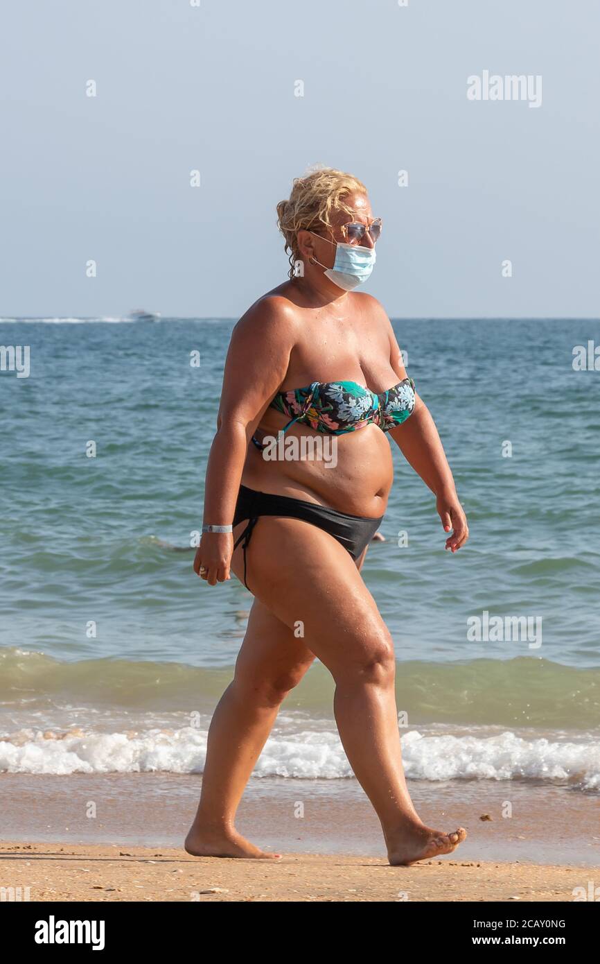 Punta Umbria, Huelva, Spagna - 7 agosto 2020: Donna in sovrappeso che cammina sulla spiaggia indossando maschere protettive o mediche. Nuova normalità in Spagna con Foto Stock