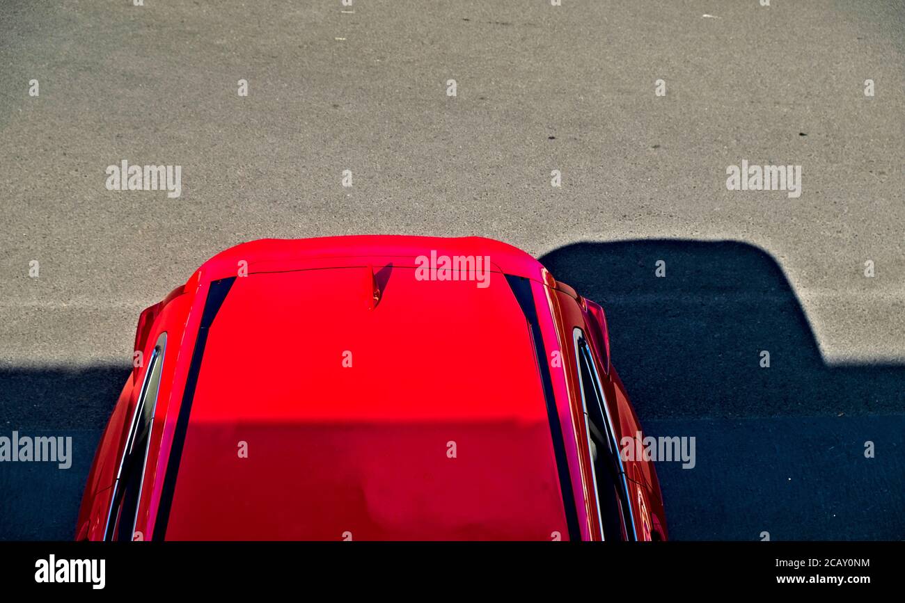 Auto suv rossa moderna parcheggiata in un parcheggio in asplalt nero, vista dall'alto della sezione posteriore, aree di sole e ombra. Foto Stock