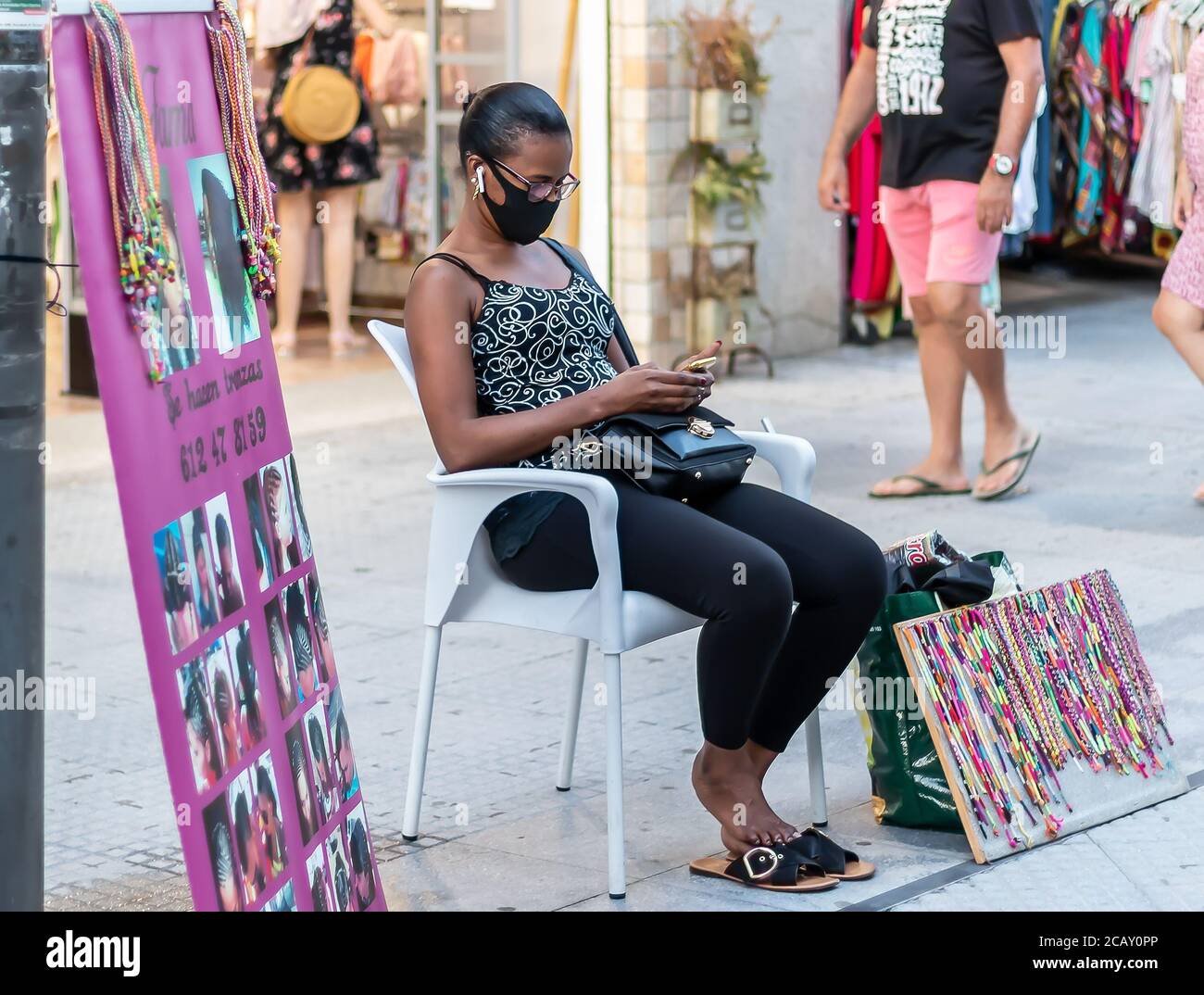 Punta Umbria, Huelva, Spagna - 7 agosto 2020: Una donna migrante africano strada laterale parrucchiere. Qui il parrucchiere è in attesa di creare trecce in h. Foto Stock