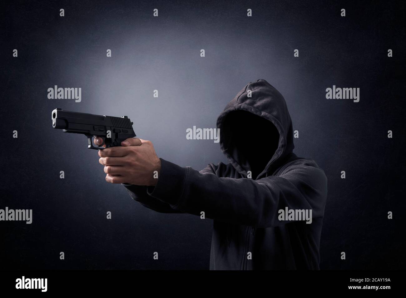 Uomo incappucciato con una pistola nel buio Foto Stock