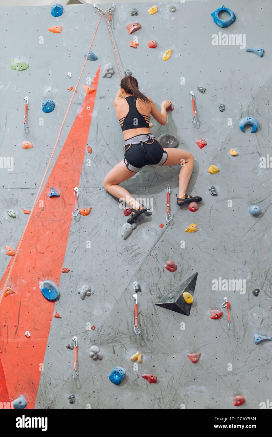 Giovane donna flessibile che si arrampica sulla parete in palestra, vista posteriore foto a lunghezza intera. Hobby, stile di vita, tempo libero Foto Stock