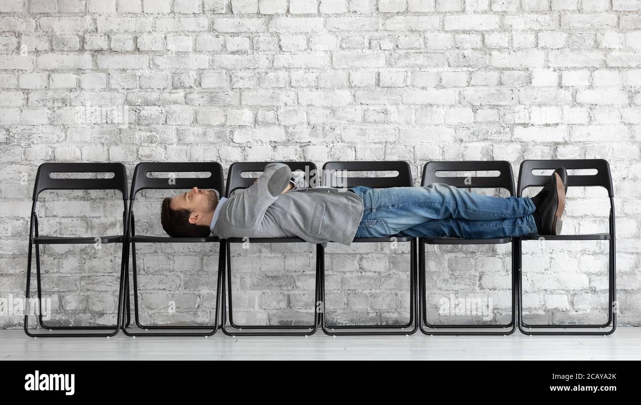 Annoiato candidato esausto sdraiato su sedie da ufficio, in attesa di intervista Foto Stock