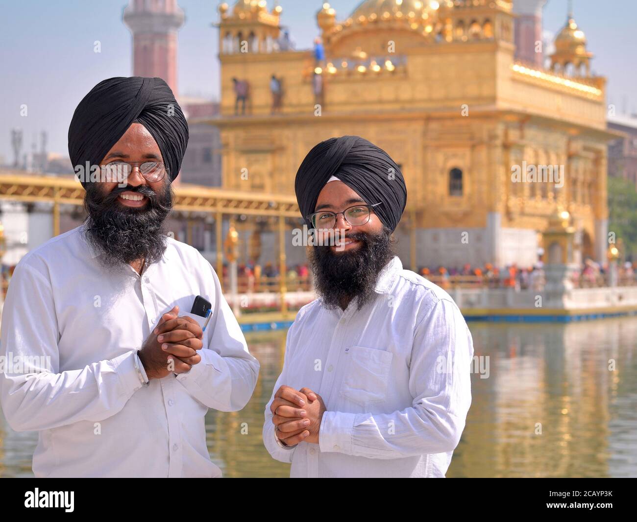 Due giovani guide del tempio Sikh si piegano le mani e sorridono per la macchina fotografica di fronte al Tempio d'Oro (Sri Harmandar Sahib). Foto Stock