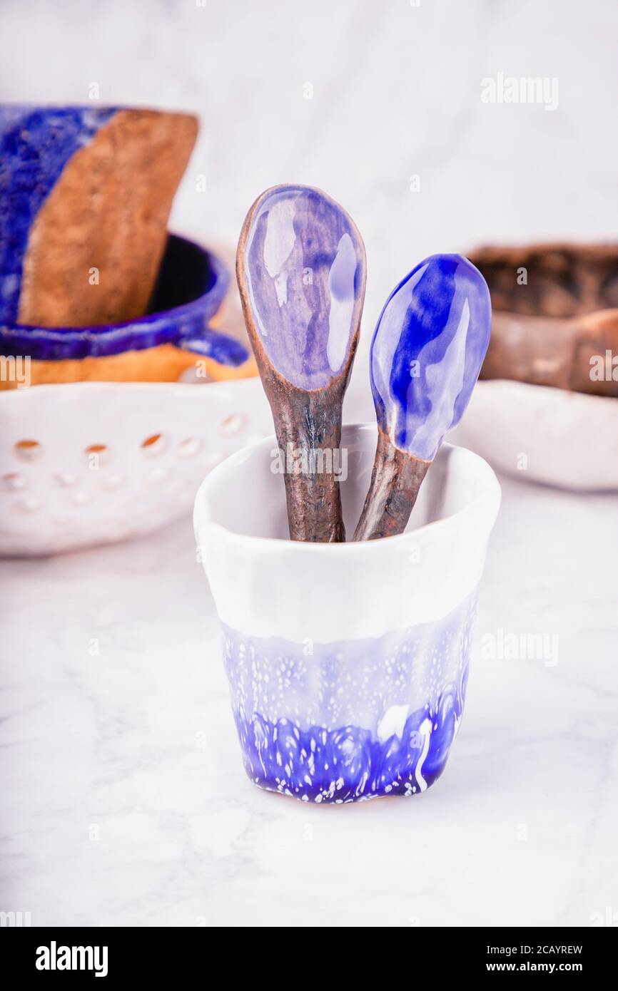 Ceramica su sfondo di marmo bianco. Colori bianco, blu e marrone. Tazze, cucchiai, ciotole. Fatto a mano Foto Stock