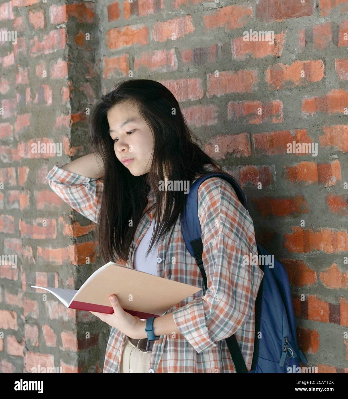Donna asiatica che legge un libro con sfondo muro di mattoni Foto Stock
