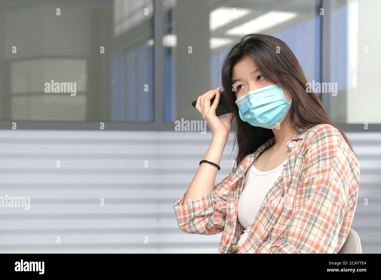 Donna asiatica che indossa la maschera fce ha messo il suo cellulare alle sue orecchie. Ascoltare la posta vocale. Foto Stock