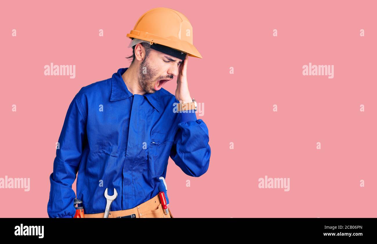 Giovane uomo ispanico che indossa un operaio uniforme sbadigli stanco coprendo metà faccia, occhio e bocca con la mano. Faccia fa male nel dolore. Foto Stock
