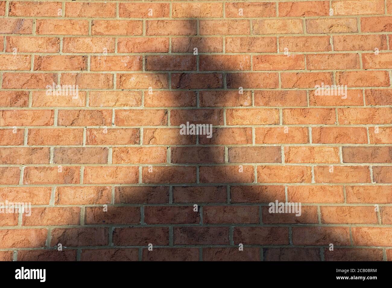 Riflessione trasversale su un muro e simbolo religioso, luce tardo pomeriggio su uno sfondo di mattoni. Foto Stock