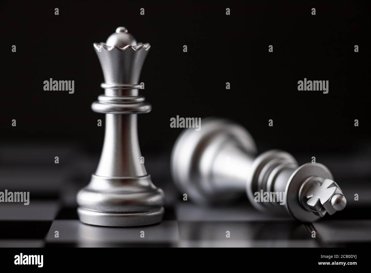 La regina d'argento in piedi e il re che cade in gioco sulla scacchiera Foto Stock