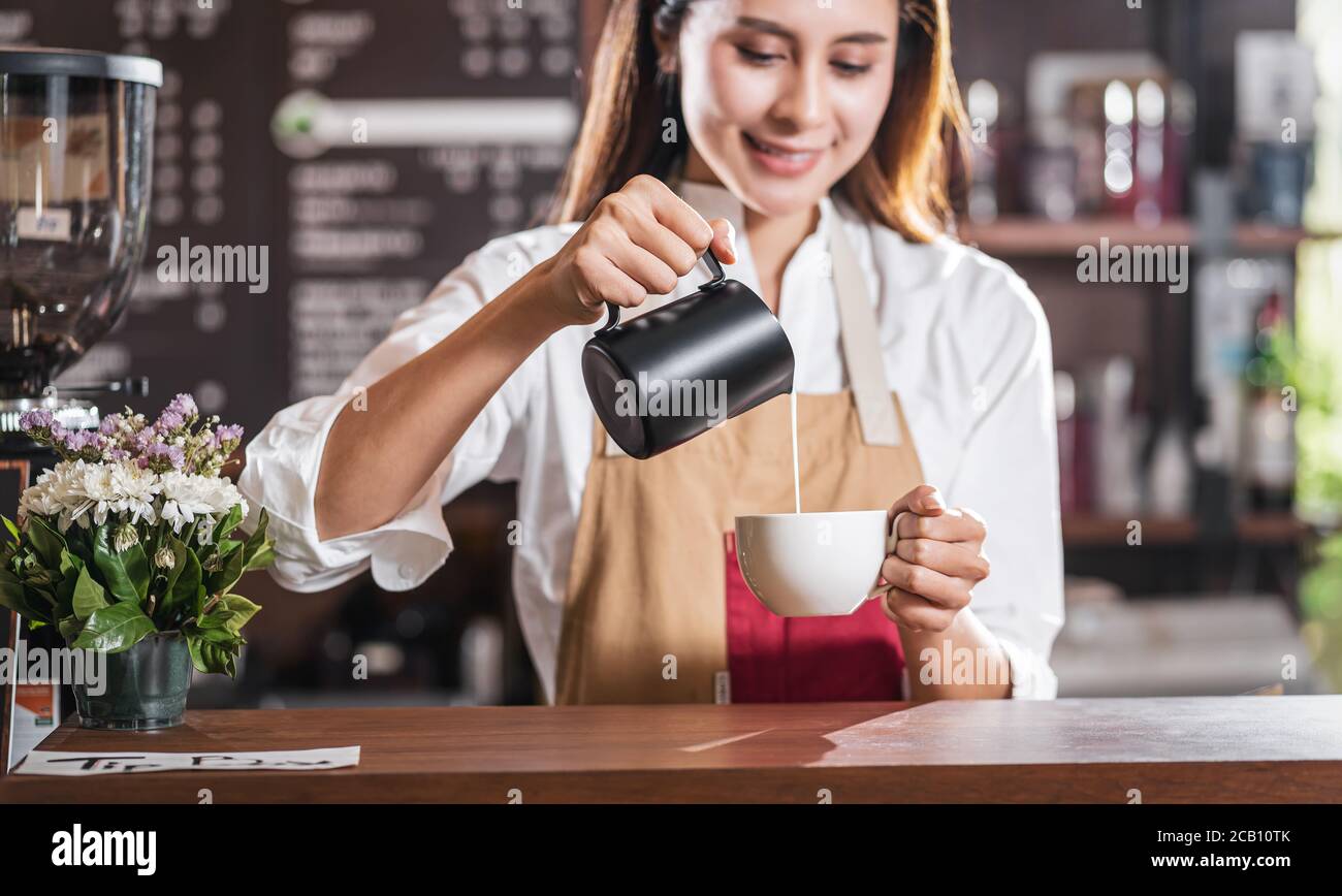 Barista asiatico versare il latte nella tazza di caffè, espresso con latte o cappuccino per ordine del cliente in caffetteria, titolare di piccola azienda e sta Foto Stock Barista asiatico versare il latte nella tazza di caffè, espresso con latte o cappuccino per ordine del cliente in caffetteria, titolare di piccola azienda e sta Foto Stock