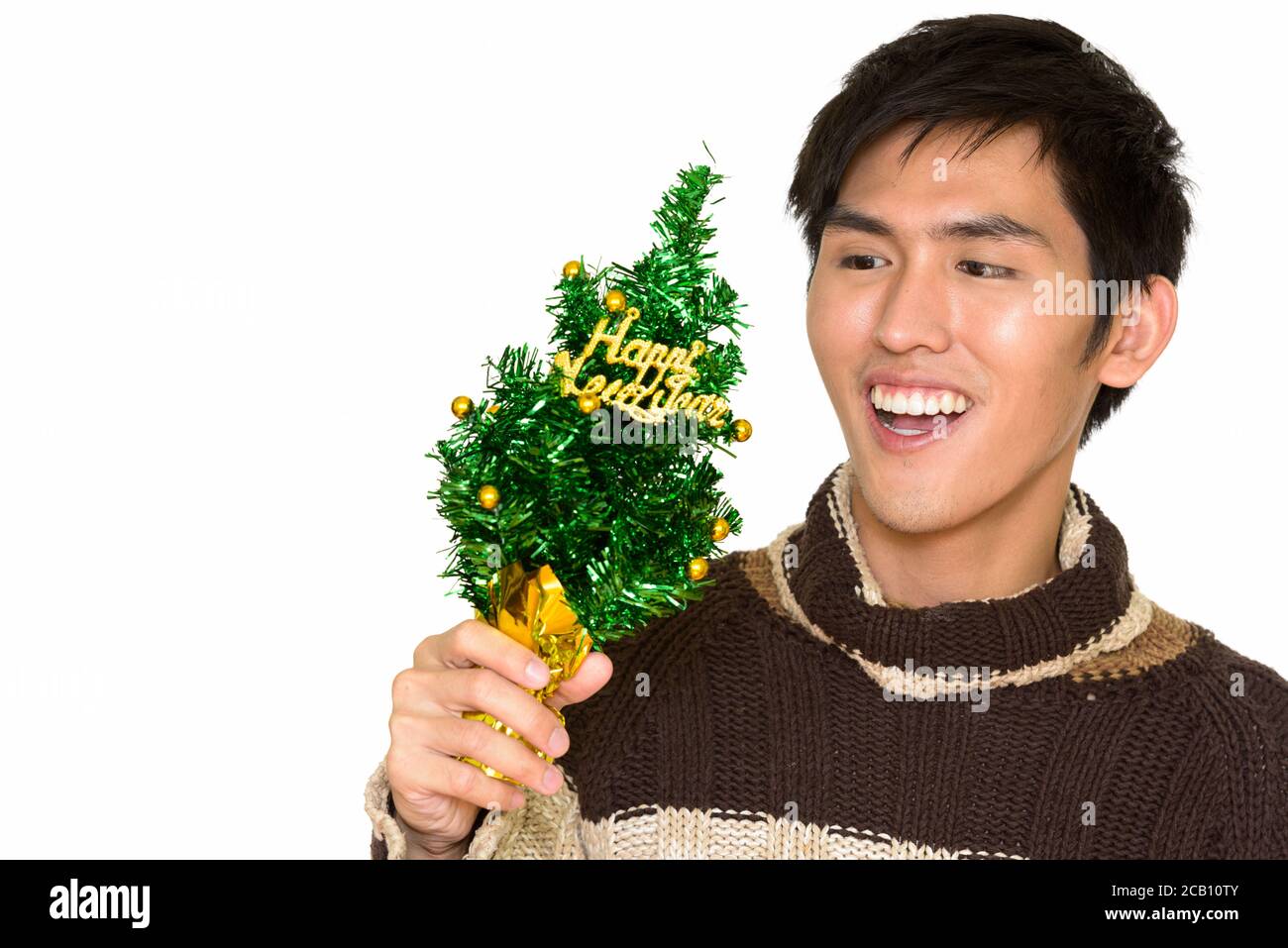Studio di giovane bell'uomo asiatico che tiene felice nuovo Albero anno e sorridente isolato su sfondo bianco Foto Stock