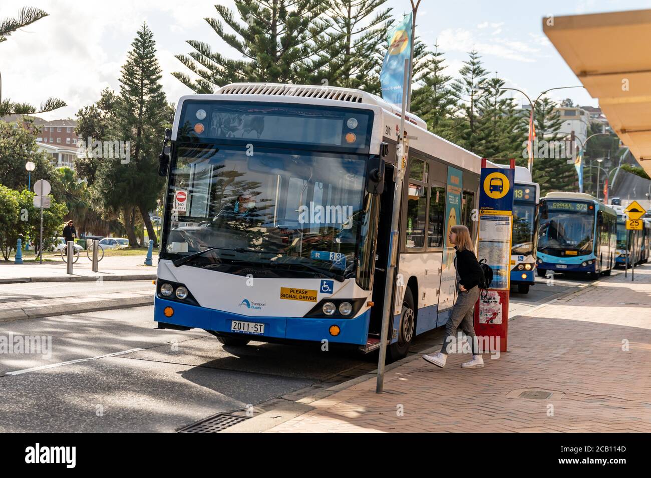 Un autobus parcheggiato al terminal degli autobus e un giovane pendolari Avvicinandosi al conducente per informazioni a Coogee Beach su un pomeriggio invernale soleggiato Foto Stock