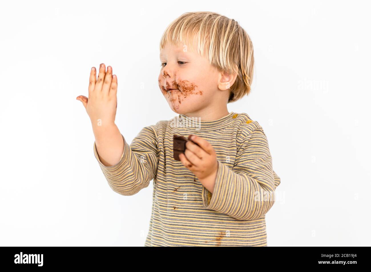 Carino biondo toddler mangiare cioccolato bar con grande piacere, sfondo bianco, Polonia Foto Stock