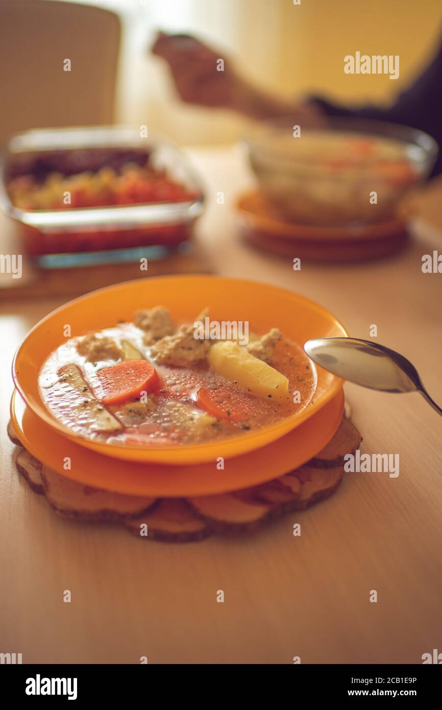 Zuppa con polpette, patate e carote in un piatto arancione su un tavolo di legno Foto Stock