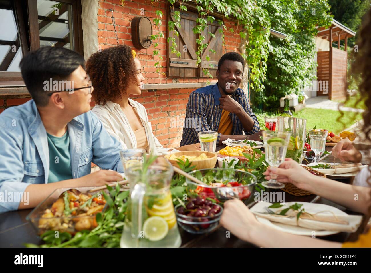 Ritratto di un gruppo multietnico di amici che si godono la cena insieme all'aperto mentre si siede al tavolo sulla terrazza aperta, concentrarsi su sorridente uomo afro-americano condividere storie, spazio di copia Foto Stock