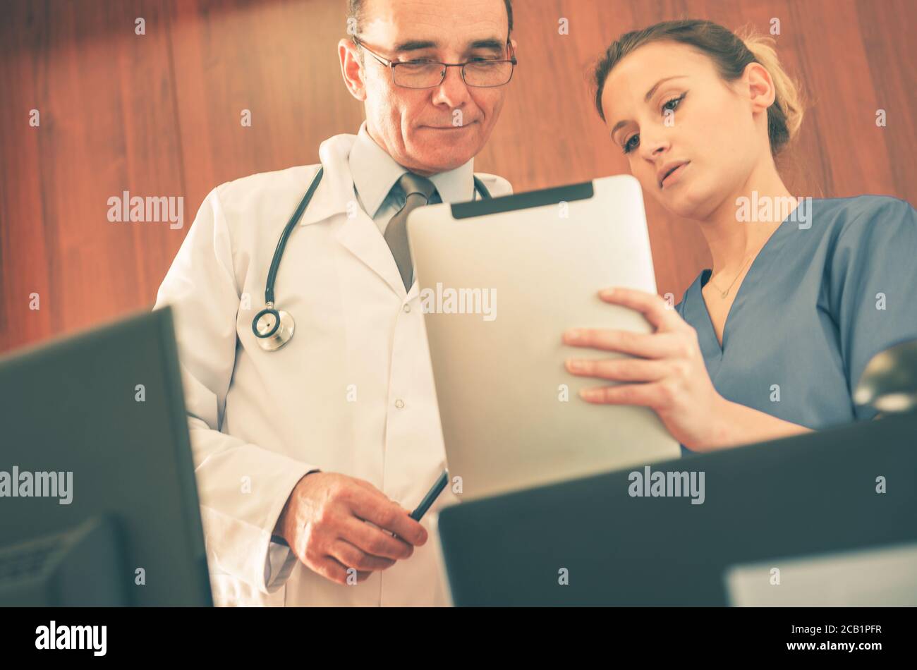 Medico e infermiere guardando la cartella paziente su un dispositivo elettronico e discutendo il trattamento appropriato. Foto Stock