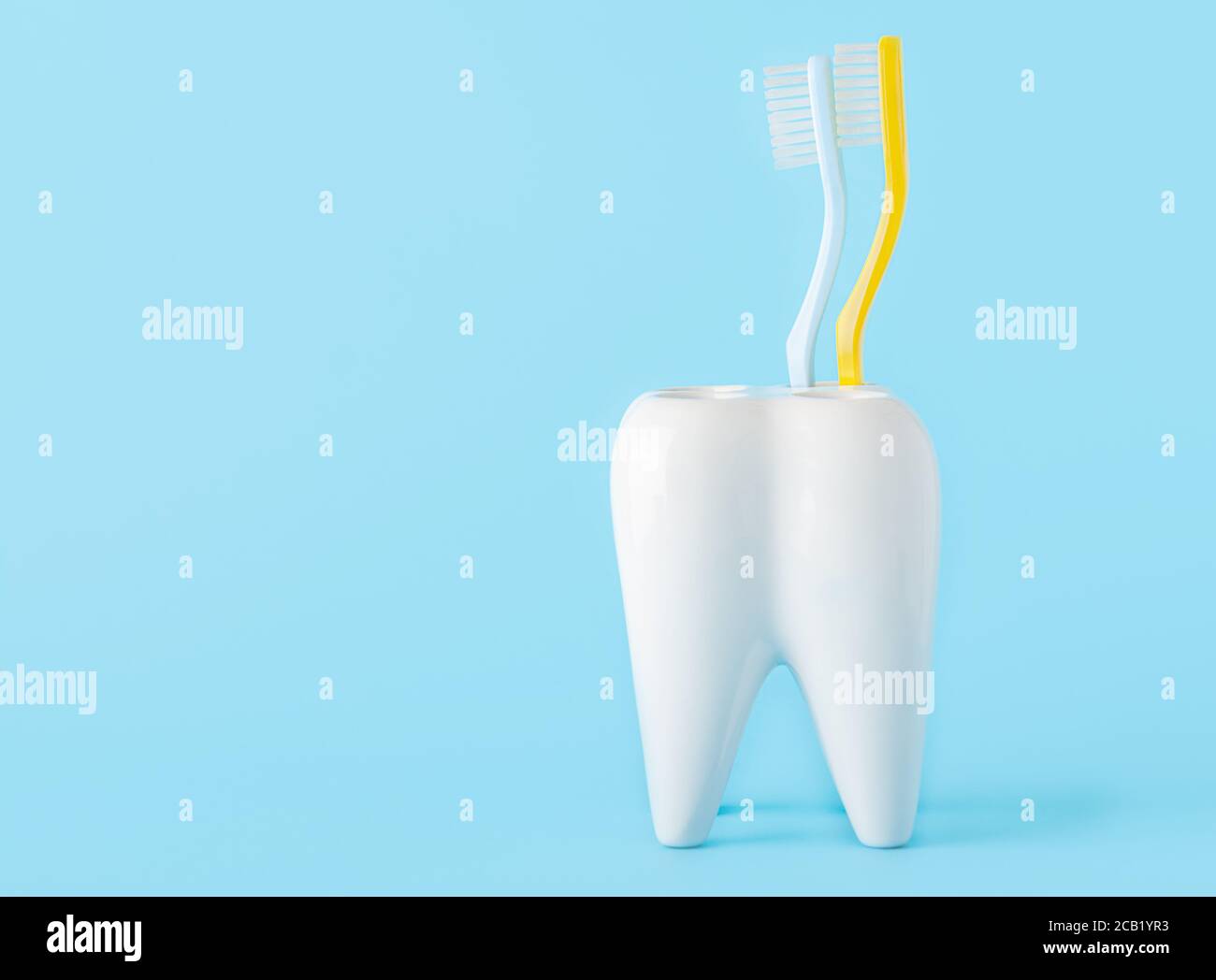Due spazzolini da denti in un bicchiere a forma di dente sopra uno sfondo blu Foto Stock