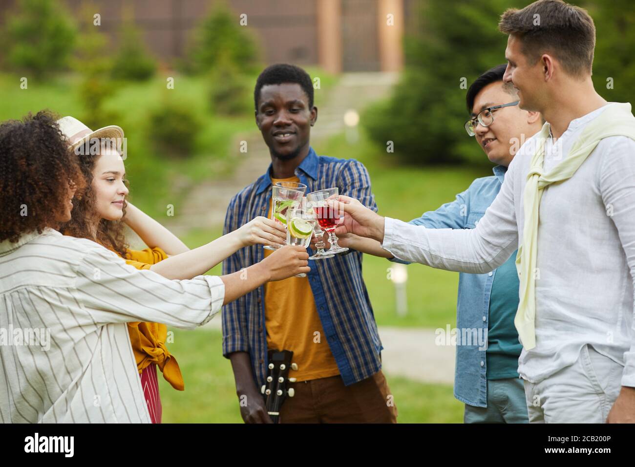 Gruppo multietnico di persone che si affina bicchieri da cocktail e tostano mentre si gusta una festa all'aperto in estate Foto Stock