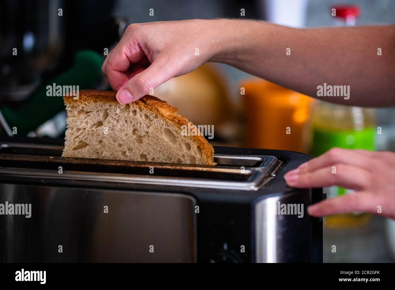 Mani ragazza tira in tradizionale fetta di pane. Mano femminile che mette il pane fresco integrale nel tostapane in cucina. Sfocare gli oggetti da cucina di sfondo. Foto Stock