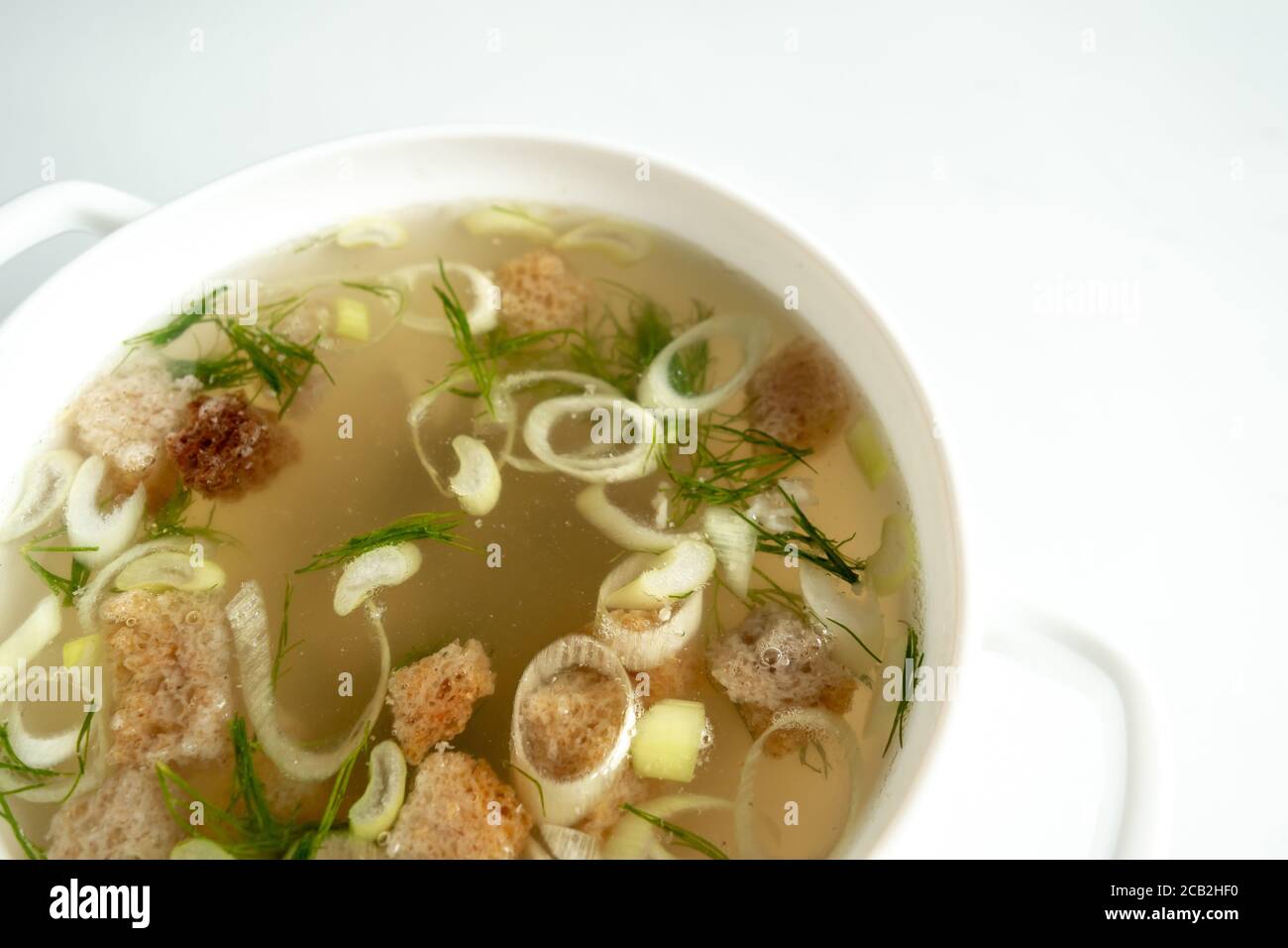 Brodo di carne fatto in casa in un tureen con aneto, cipolle e crostini su fondo bianco. Concetto di cibo sano. Dieta di Paleo. Primo piano. Spazio di copia Foto Stock