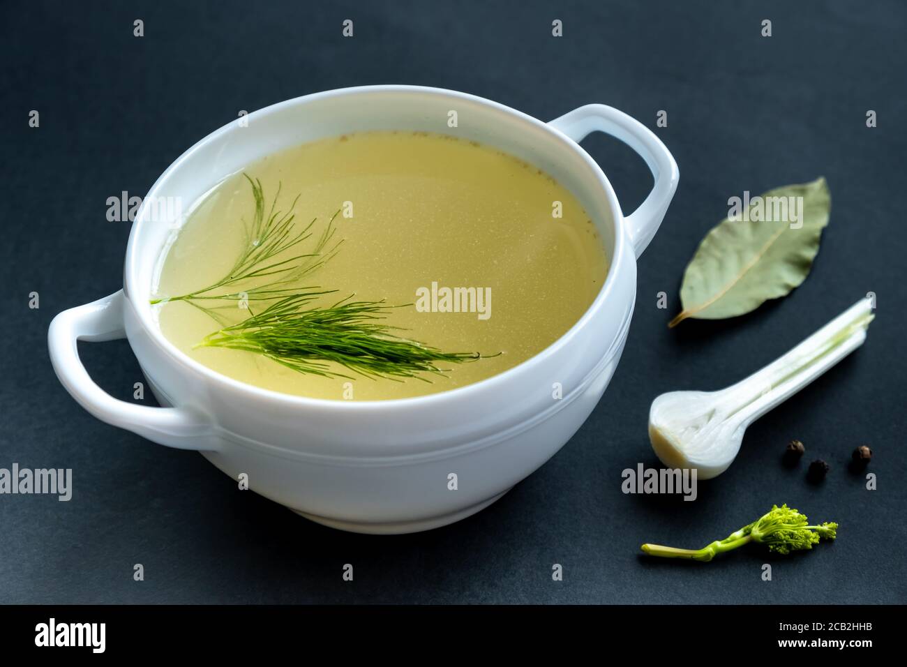 Brodo fatto in casa di ossa di carne in un tureen, verdure e condimenti, su sfondo nero. Alimentazione sana concept.Paleo dieta. Messa a fuoco selettiva.primo piano. Foto Stock