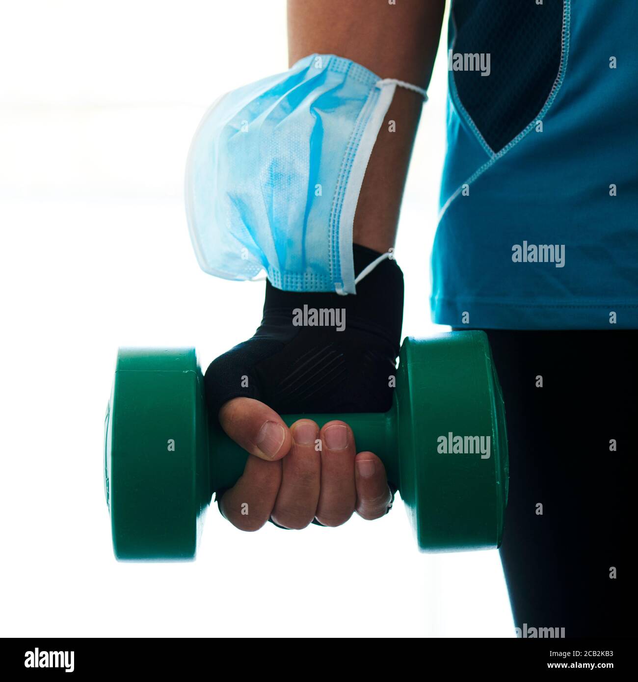 primo piano di un giovane caucasico in palestra, indossando abbigliamento sportivo, utilizzando un manubri e indossando la maschera chirurgica nel braccio mentre non lo indossa Foto Stock