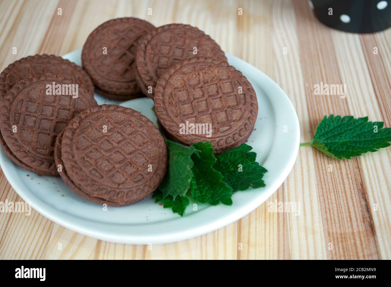 Porzioni di biscotti al cioccolato su sfondo di legno. Impilare i biscotti con scaglie di cioccolato. Biscotti al cioccolato sul piatto e una tazza nera in cerchi bianchi dopo Foto Stock