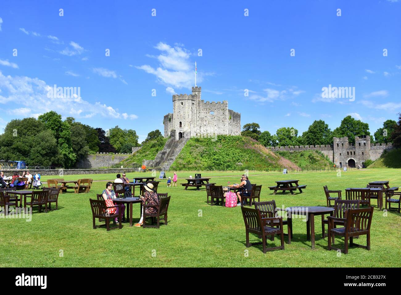 Le persone che godono del sole e bevono un drink ai tavoli socialmente distanziati nei giardini del Castello di Cardiff, Cardiff, Galles Foto Stock