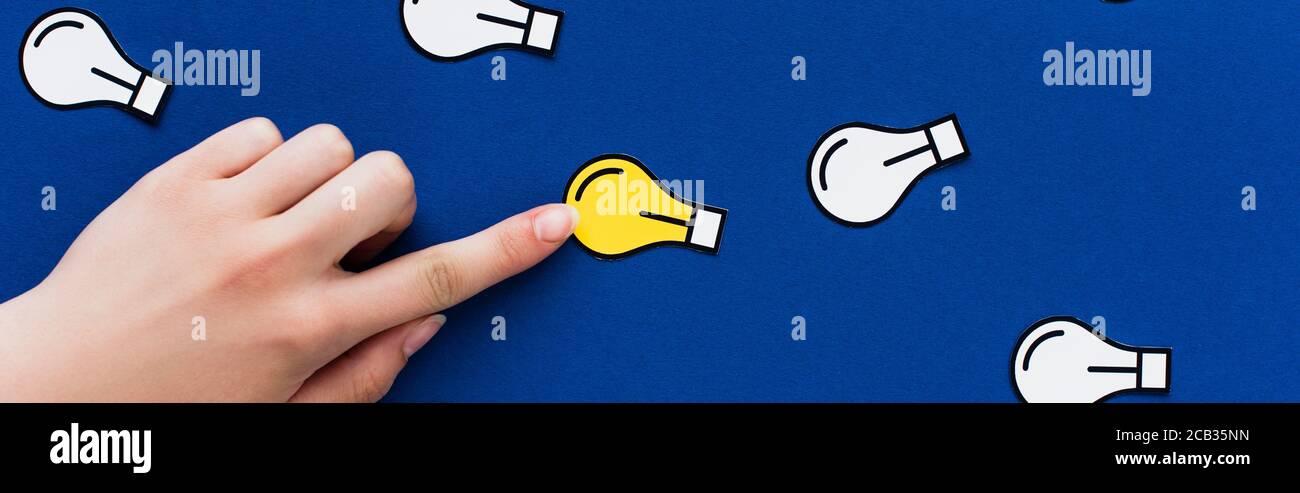 vista ritagliata della mano che punta alla lampadina della luce di carta su sfondo blu, concetto di business Foto Stock