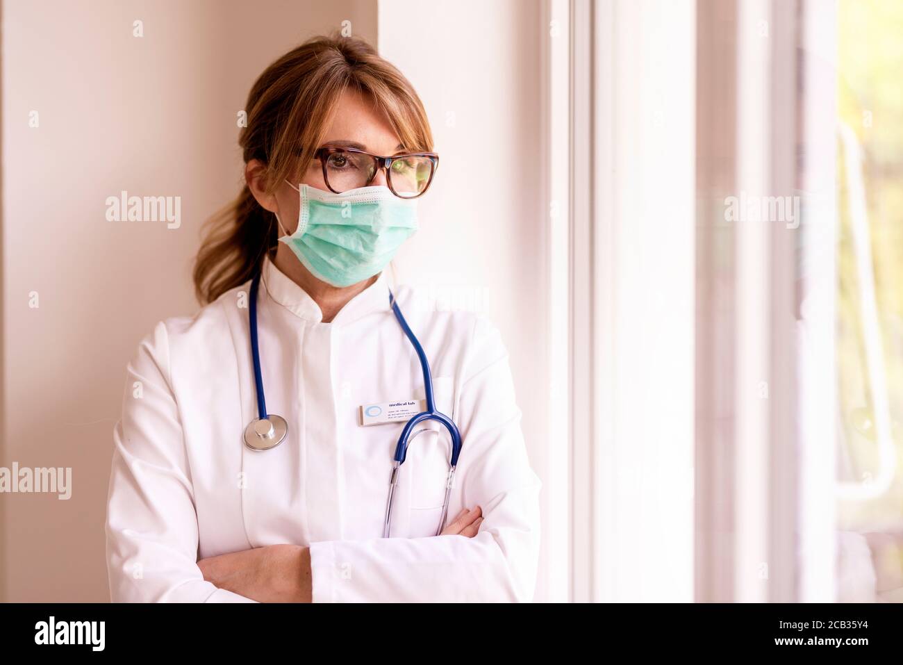 Medico femminile che indossa maschera facciale e guardando caregived mentre guarda fuori la finestra durante la diffusione del coronavirus rapidamente nel paese. Foto Stock