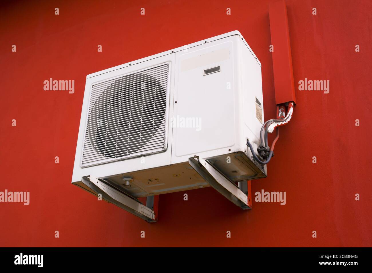 Aria condizionata - dispositivo elettronico per il raffreddamento di temperature calde e calde. Il condizionatore d'aria bianco si trova sulla parete rossa Foto Stock