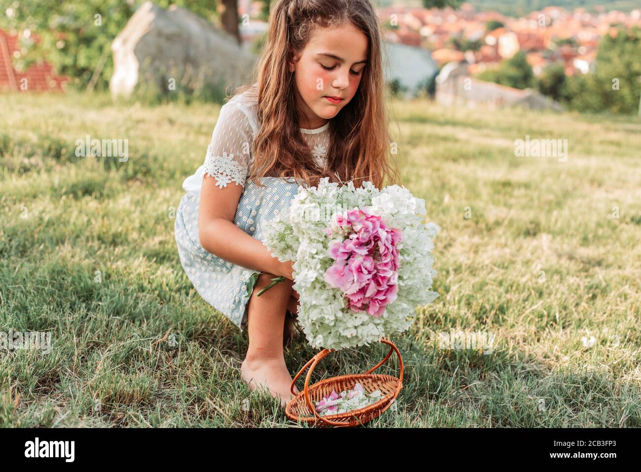Bambina bionda riccia raccolta fiori da terra nel suo piccolo cesto, facendo un bouquet Foto Stock