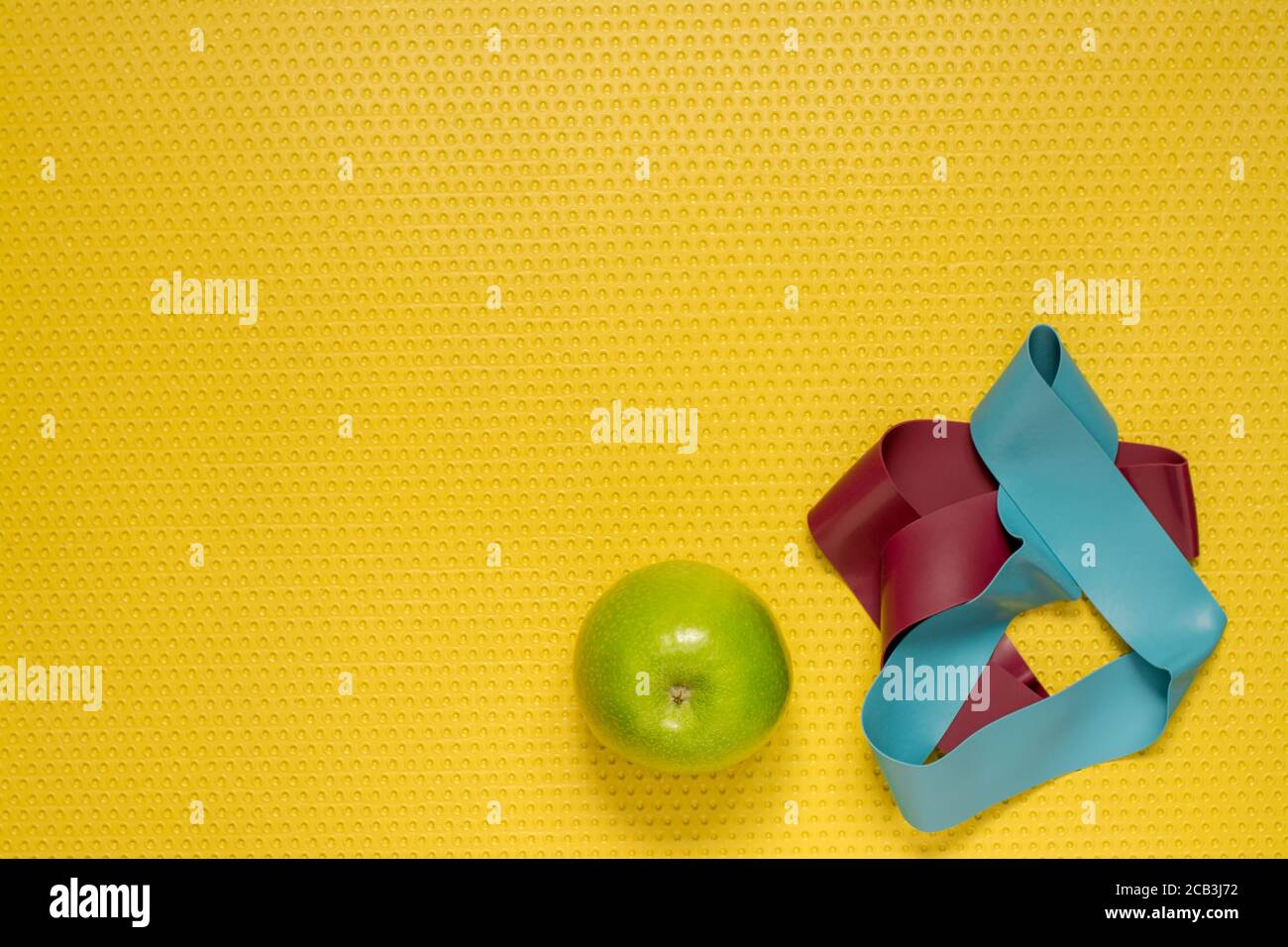 Vista dall'alto di una mela verde e di una fascia Pilates sul tappetino giallo. Sport a casa, yoga e Pilates pratica Foto Stock