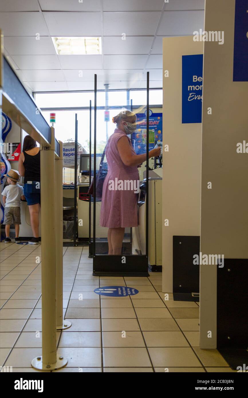 Una donna che indossa una maschera mentre si usa l'auto checkout in un supermercato Foto Stock