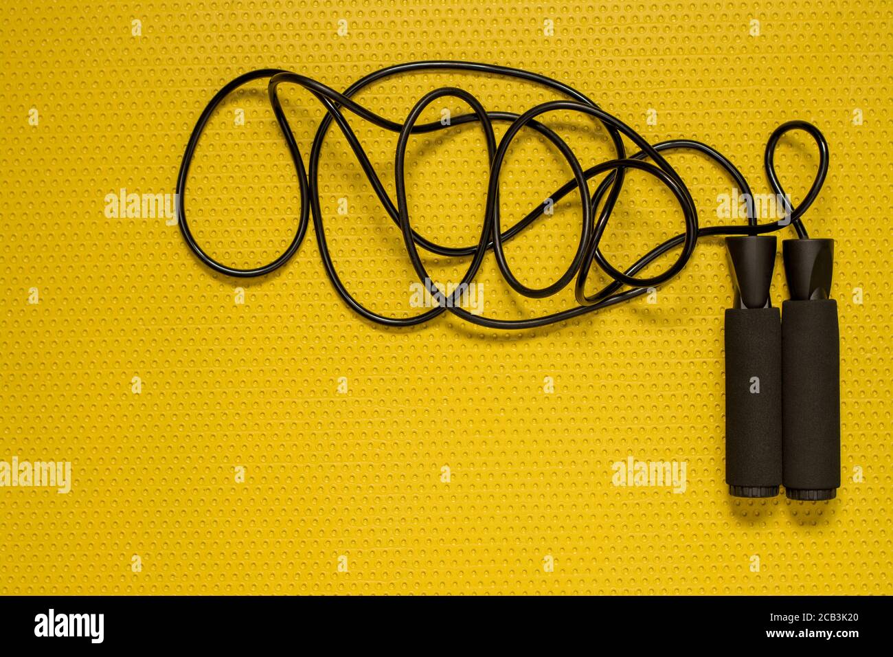 Vista dall'alto di una fune di salto sul tappetino giallo. Sport a casa, allenamento fitness Foto Stock