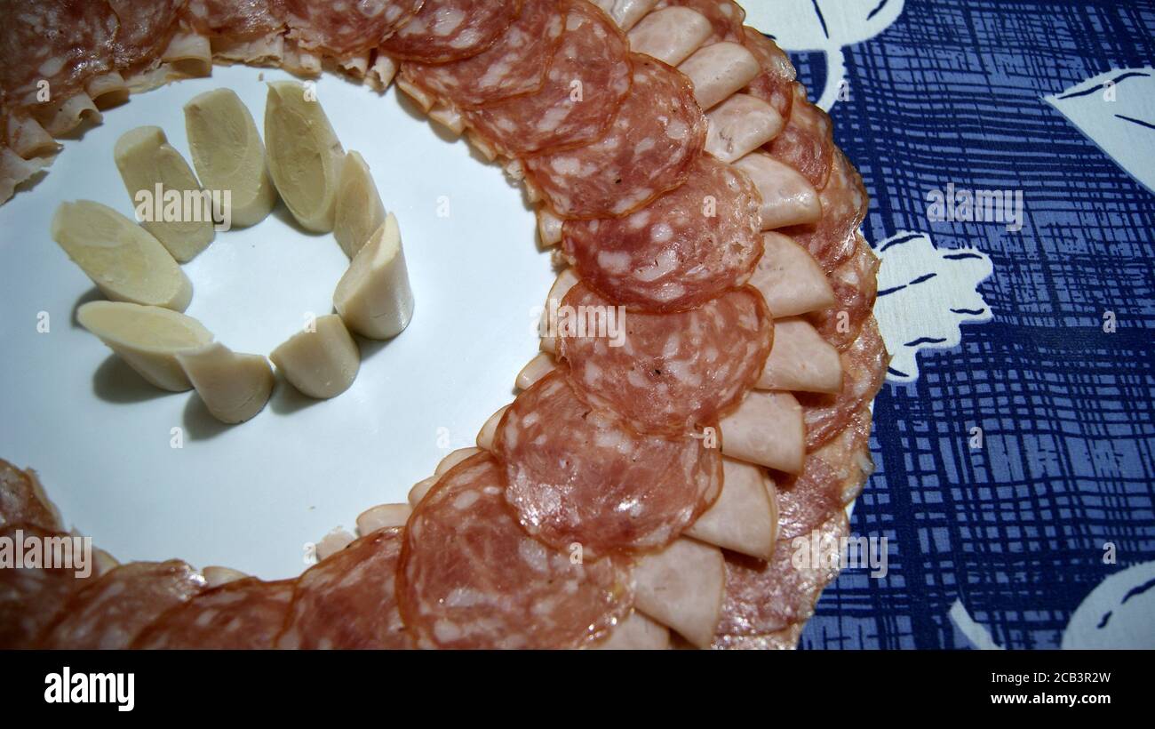 Piatto bianco decorato con salame, prosciutto e cuore di palma al centro su uno sfondo con una tovaglia blu e bianca, dettaglio, un piatto noto come il co Foto Stock