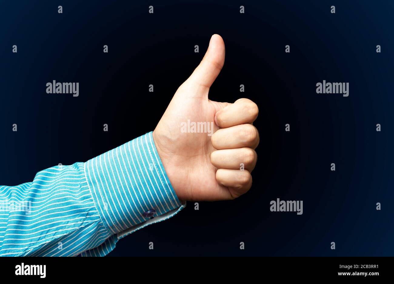 La mano di un giovane uomo sta mostrando un pollice in su, indicando che gradisce o approva qualcosa su sfondo scuro Foto Stock
