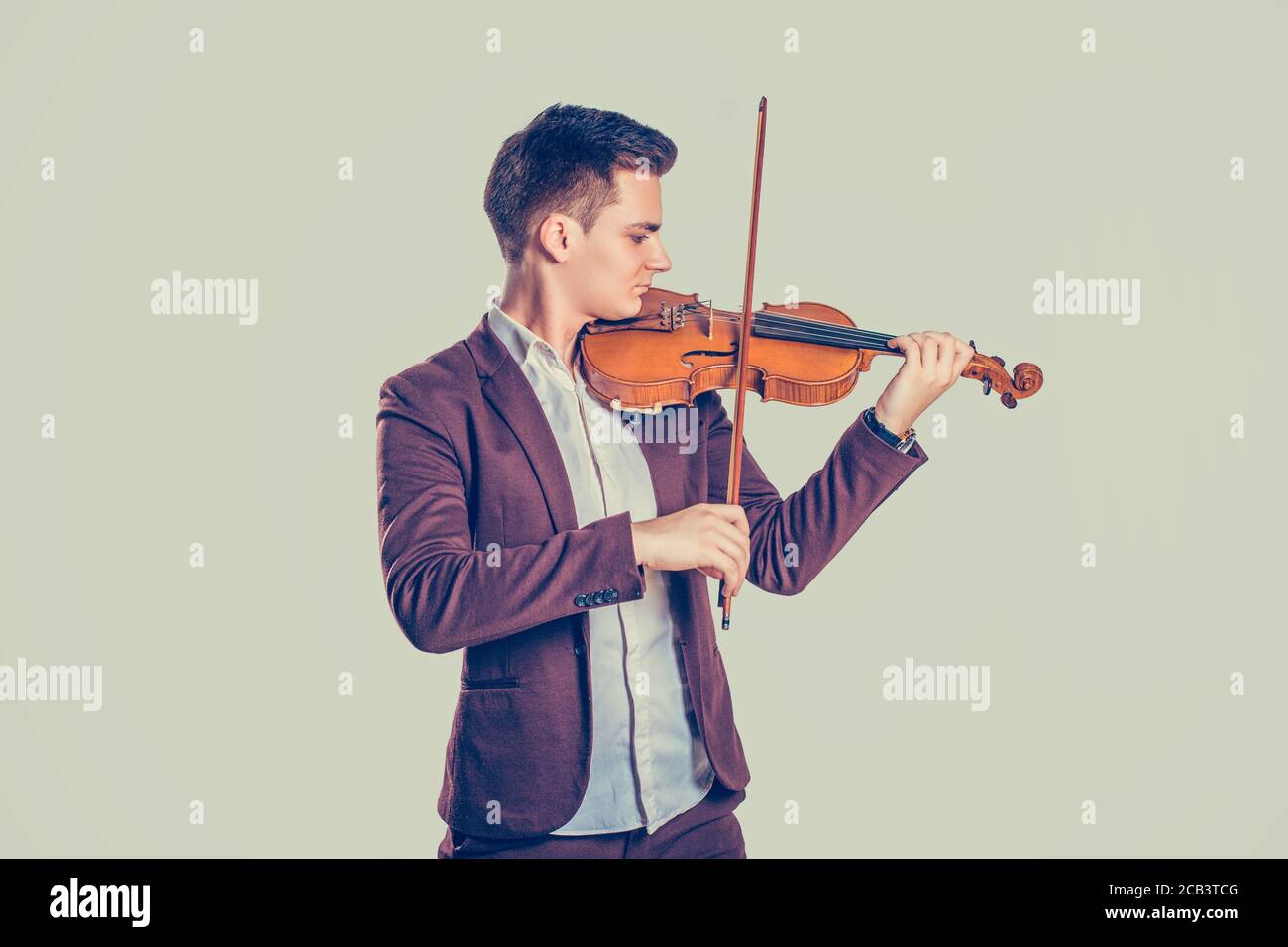 Passione musicale, concetto hobby. Giovane uomo vestito moderno ed elegante giocando su violino in legno in uno studio isolato su uno sfondo verde chiaro. H Foto Stock
