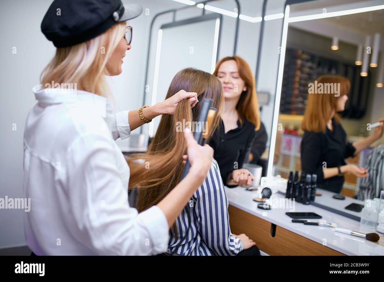 stylist professionale per capelli facendo capelli a giovane ragazza caucasica con capelli lunghi, parrucchiere attento e giovane bella cliente in salone di bellezza Foto Stock