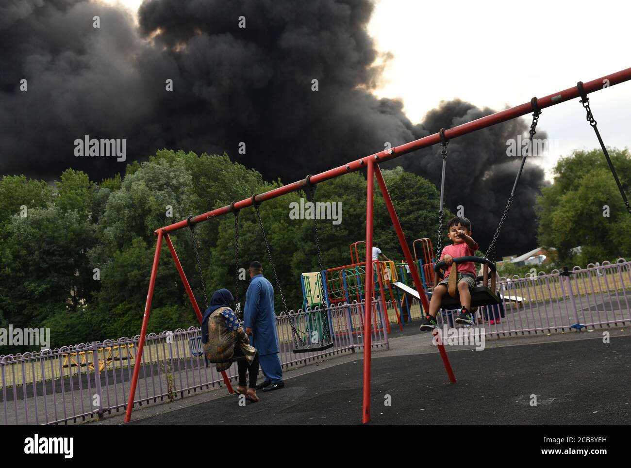 IL PERMESSO DEI GENITORI HA CONCESSO alle persone in un parco quando il fumo si sentirà in bilera da una grave bagliore in una zona industriale di Birmingham. Gli equipaggi di 10 motori antincendio stanno affrontando il fuoco. Foto Stock