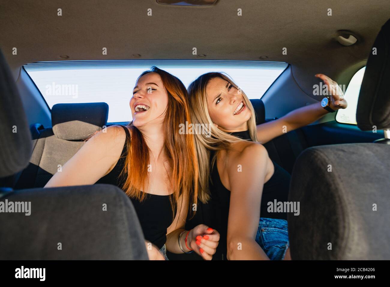 Sorridendo amici donne che si divertono, cantano e ballano all'interno del salone auto durante il viaggio su strada. Foto Stock
