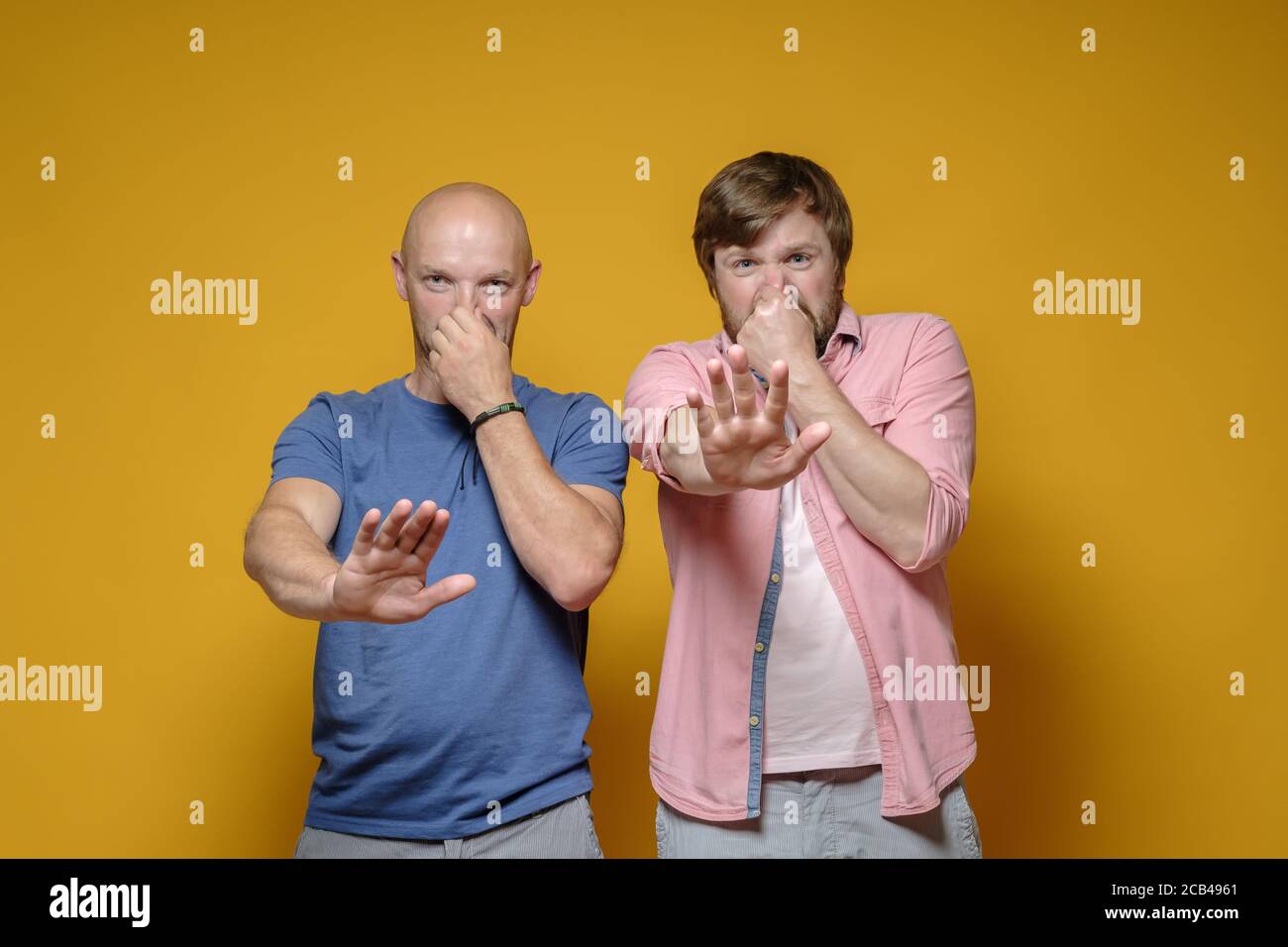Due uomini sentono un odore stinoso e disgustoso, coprono il naso con la mano e fanno un gesto di stop con il palmo. Foto Stock