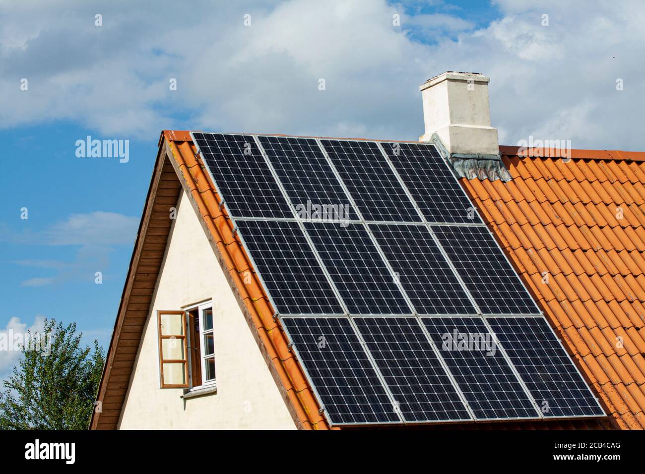 Moderni pannelli solari neri sul tetto in tegole rosse di una vecchia casa con sfondo blu cielo. Foto Stock