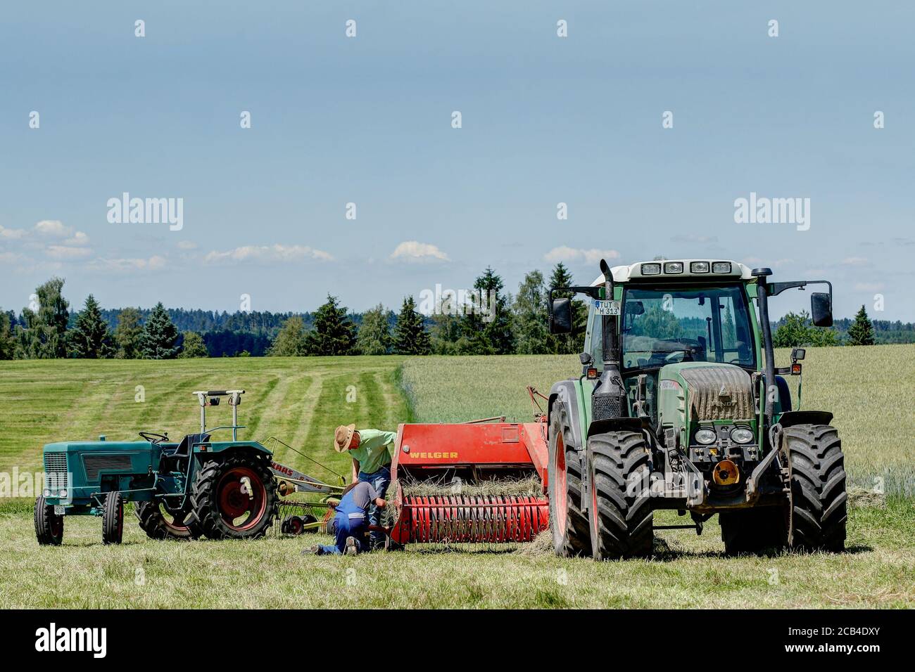 Trossingen, Germania, 06/25/2020. Due agricoltori che riparano una pressa Welger sul campo. Il moderno trattore Fendt Vario 313 e la vecchia tecnologia si incontrano. Foto Stock