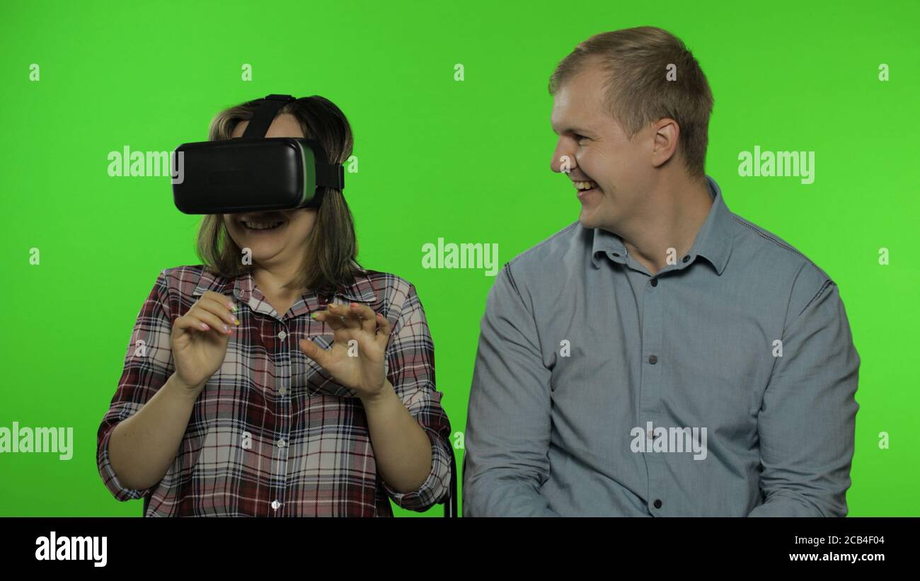 Uomo e donna che usano il casco del visore VR per giocare. Guy spaventa la  ragazza durante la visione di un video 3D 360 in realtà virtuale. Famiglia  isolata su sfondo verde